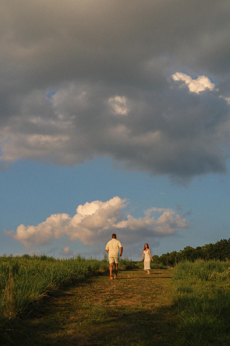 Couple walking up a grass track under a wide sky of broken cloud