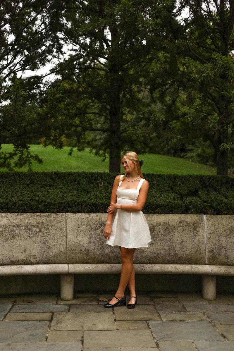 Senior portrait beside a curved stone bench in front of a clipped hedge