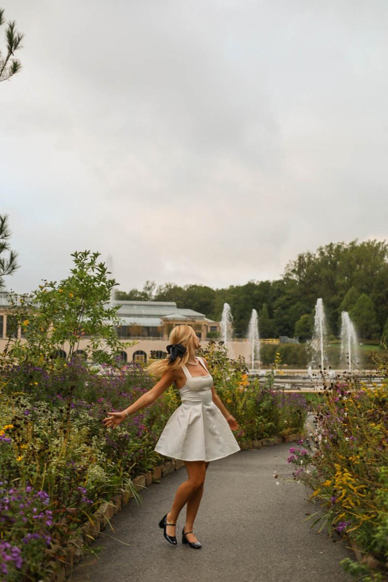 A young woman turning on a narrow path between deep beds of late-summer flowers