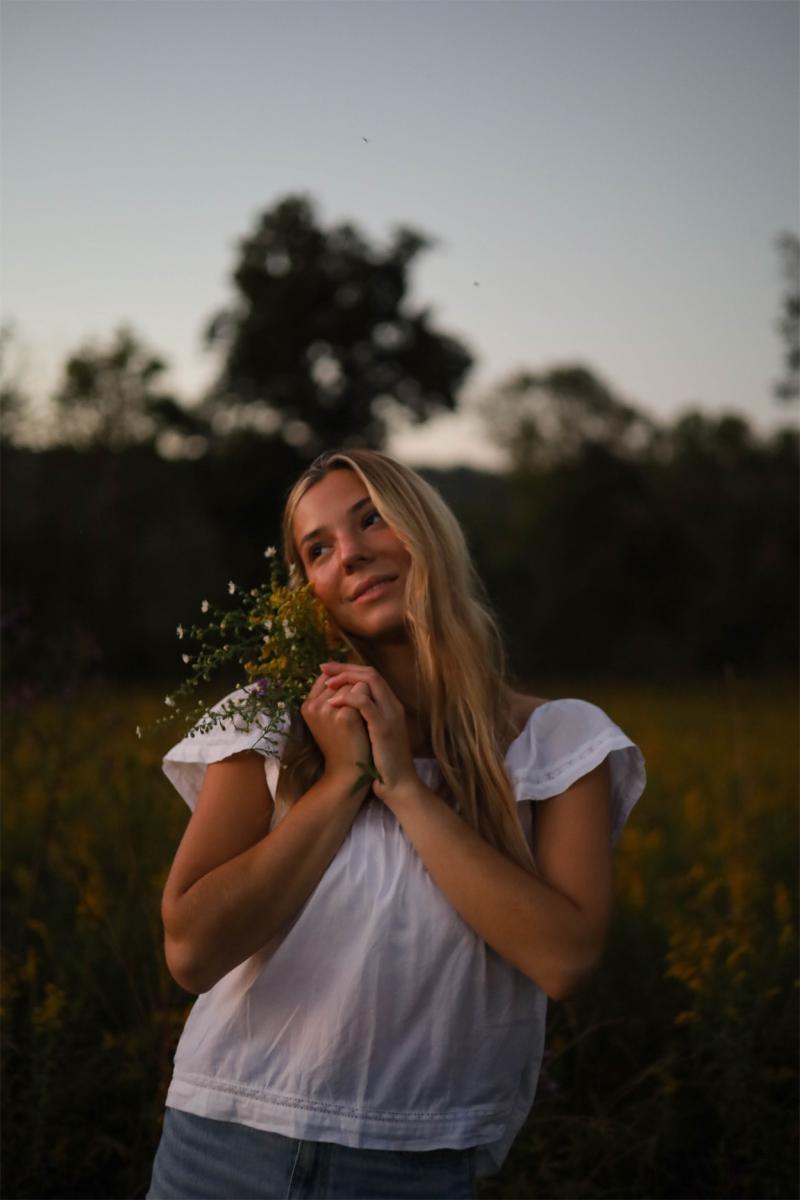 Young woman holding a handful of wildflowers in a meadow at dusk
